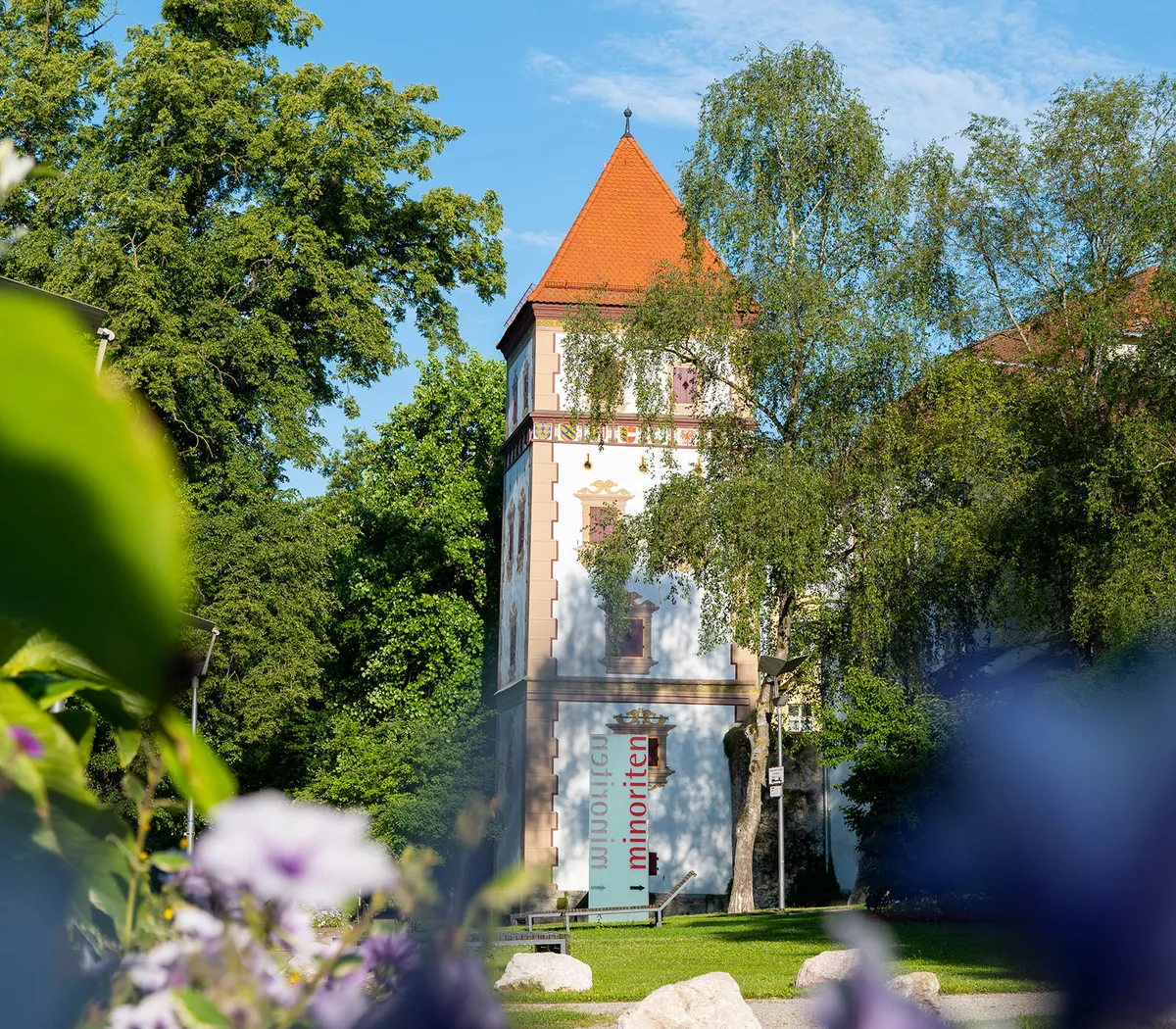 Der historische Wasserturm im Stadtgarten Wasserturm Am Zwinger hat ein rotes Dach und steht idyllisch zwischen Bäumen und Blumen.